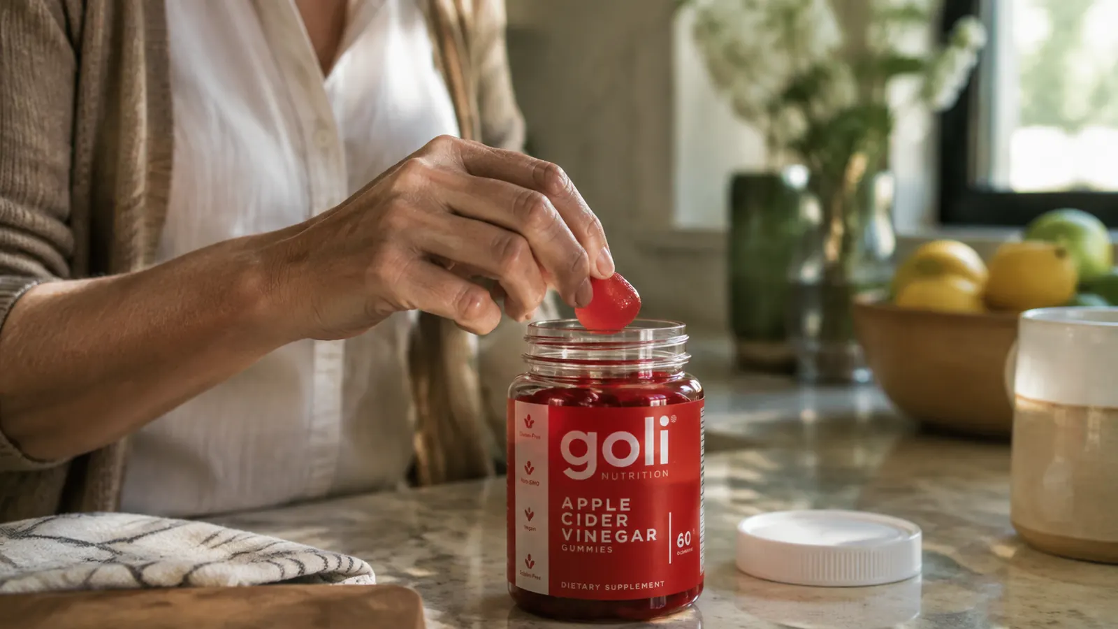 A hand lifting one gummy out of the Goli vinegar gummy jar at the kitchen counter